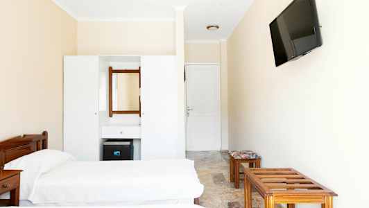 Hotellihuoneen sisustus, jossa kaksi erillistä sänkyä, lipasto peilillä ja seinään kiinnitetty TV. (Tekoälyn luoma teksti)