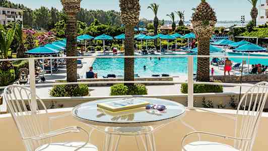 Parveke, jossa lasipöytä ja tuoleja, näkymä uima-altaalle, jossa aurinkotuoleja ja palmuja. (Tekoälyn luoma teksti)