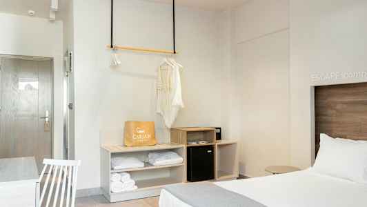 Hotellihuone, jossa on pedattu sänky, vaatekaappialue ja pöytä tuolilla. (Tekoälyn luoma teksti)