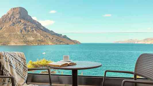 Pöytä, jossa on kuppi ja kirja, sijaitsee parvekkeella merelle ja vuorelle päin avautuvalla näkymällä. (Tekoälyn luoma teksti)