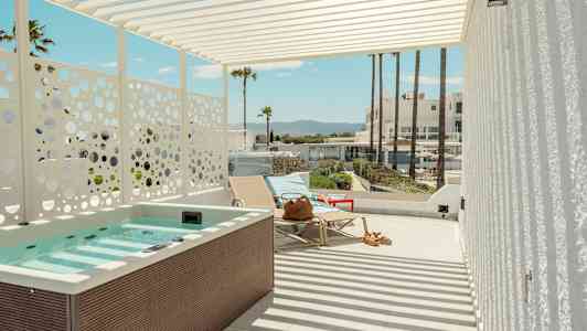 Terassi, jossa poreallas, aurinkotuoleja ja näkymä palmuihin ja rakennuksiin taustalla. (Tekoälyn luoma teksti)