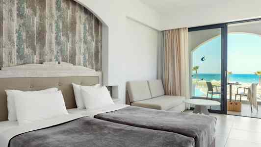 Hotellihuone, jossa kaksi vuodetta, oleskelutila ja näkymä merelle lasioven kautta. (Tekoälyn luoma teksti)