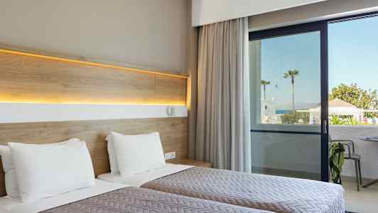 Hotellihuone, jossa kaksi erillistä vuodetta ja näkymä patiolle sekä merelle taustalla. (Tekoälyn luoma teksti)