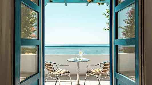 Näköala avointen ovien kautta parvekkeelle, jossa on merinäköala, sisältäen pöydän ja kaksi tuolia. (Tekoälyn luoma teksti)