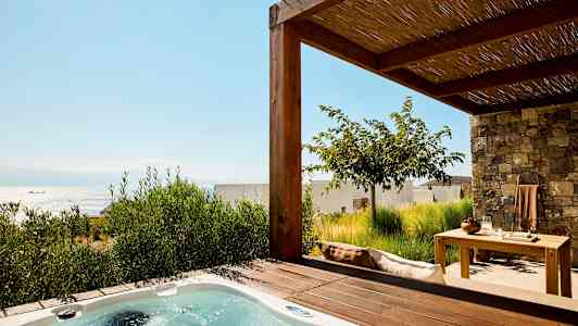 Kuva terassista, jossa on poreallas ja puutarhakalusteet, taustalla näkyy meri. (Tekoälyn luoma teksti)