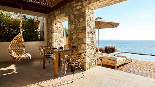 Terassi, jossa on pöytä, tuolit, riippuva istuin ja aurinkotuoleja meren äärellä. (Tekoälyn luoma teksti)