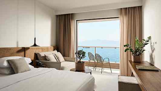 Hotellihuone, jossa on sänky, sohva ja näkymä merelle parvekkeelta. (Tekoälyn luoma teksti)