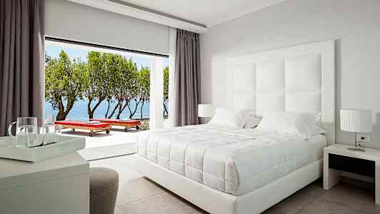 Tyylikäs hotellihuone, jossa on valkoinen parivuode ja näkymä merelle. (Tekoälyn luoma teksti)