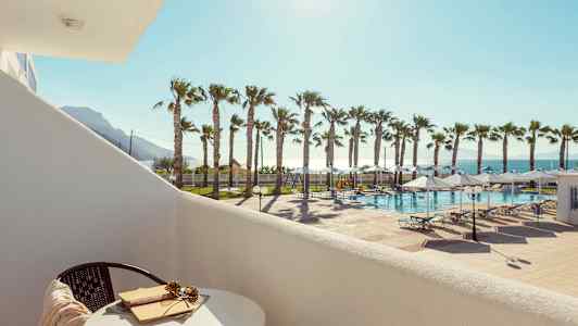 Näkymä parvekkeelta uima-altaalle, aurinkotuoleja ja palmuja auringonpaisteessa. (Tekoälyn luoma teksti)