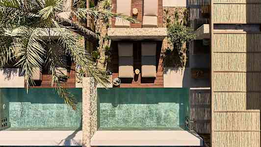 Lintuperspektiivistä kuvattuna aurinkotuoleja ja kaksi uima-allasta, palmu vieressä. (Tekoälyn luoma teksti)