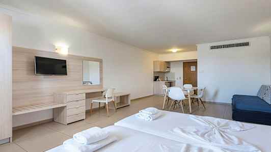 Hotellihuone, jossa on sänky, kirjoituspöytä, televisio ja ruokailutila keittiövälineillä. (Tekoälyn luoma teksti)