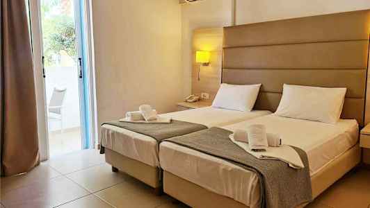 Hotellihuone, jossa on kaksi erillistä sänkyä, yöpöytä ja ilmastointilaite seinällä. (Tekoälyn luoma teksti)