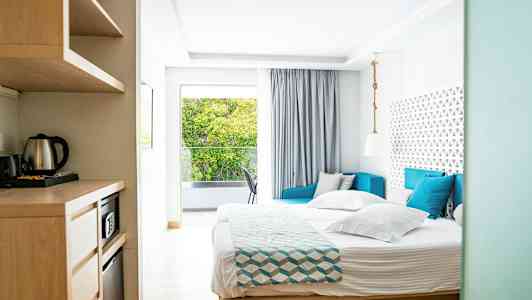 Kuva valoisasta hotellihuoneesta, jossa sänky, sohva ja ikkuna, josta näkymä. (Tekoälyn luoma teksti)