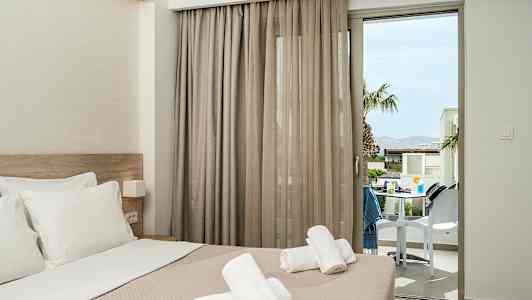 Hotellihuone, jossa petausvuode ja sen päällä olevat pyyhkeet, parvekkeen ovi avautuu terassille. (Tekoälyn luoma teksti)