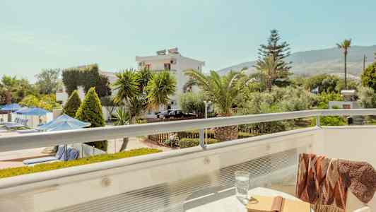 Parveke, jossa pöytä, kirja ja lasi; näkymä puutarhaan ja rakennuksiin. (Tekoälyn luoma teksti)