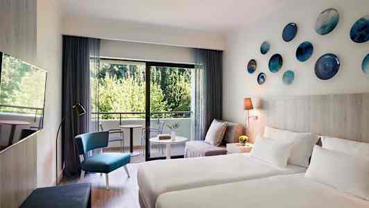 Modernisti sisustettu hotellihuone, jossa on kaksi vuodetta, istuinryhmä ja parveke näköalalla vehreyteen. (Tekoälyn luoma teksti)