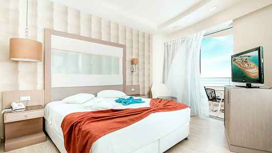 Hotellihuone, jossa iso sänky ja näkymä parvekkeelle. (Tekoälyn luoma teksti)