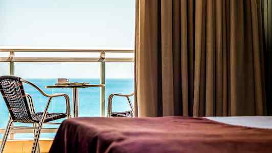 Huone, jossa ruskeat verhot, näkymä merelle ja kalustettu parveke. (Tekoälyn luoma teksti)