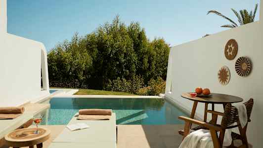 Ulkotila, jossa kaksi aurinkotuolia, pöytä juoman ja kirjan kanssa sekä uima-allas, taustalla puita. (Tekoälyn luoma teksti)