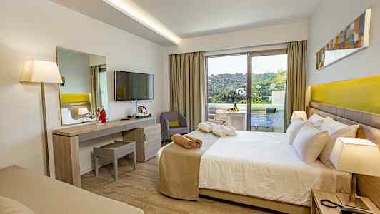 Hotellihuone, jossa on sänky, työpöytä, televisio ja parveke vihreällä näkymällä. (Tekoälyn luoma teksti)