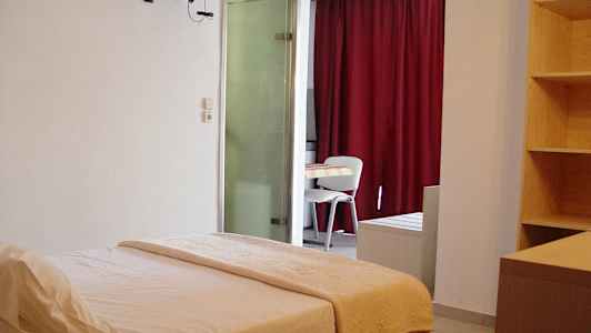 Hotellihuone, jossa on sänky, pöytä ja tuolit sekä hylly ja punaiset verhot. (Tekoälyn luoma teksti)