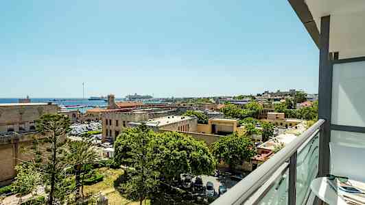 Näköala parvekkeelta kaupungille, jossa on historiallisia rakennuksia, puita ja satama veneineen. (Tekoälyn luoma teksti)