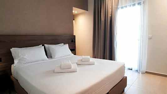 Hotellihuone, jossa on parivuode ja valkoiset lakanat, sekä sängylle asetetut taitetut pyyhkeet. (Tekoälyn luoma teksti)