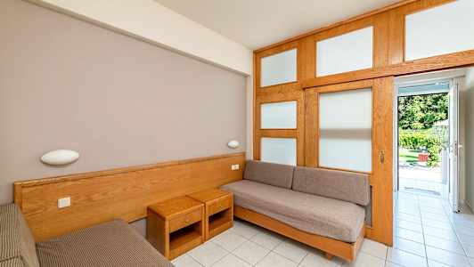 Huone, jossa on kaksi erillistä vuodetta ja puuhuonekalut, avautuu puutarhaan. (Tekoälyn luoma teksti)