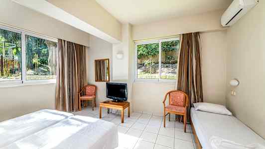 Hotellihuone, jossa on kaksi sänkyä, tuoleja, pöytä televisiolla ja suuret ikkunat. (Tekoälyn luoma teksti)