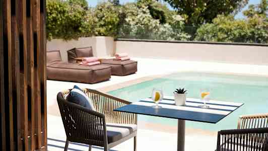 Pöytä, jossa kaksi vesilasia ja pieni kasvi uima-altaan vieressä, taustalla aurinkotuoleja. (Tekoälyn luoma teksti)