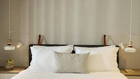 Vuode, jossa on tyynyjä ja valaistut valaisimet molemmin puolin. (Tekoälyn luoma teksti)