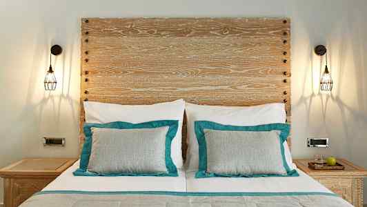 Huone, jossa sänky, jossa kaksi tyynyä turkooseilla yksityiskohdilla ja puinen pääty. Sängyn kummallakin puolella on yöpöydät valaisimineen. (Tekoälyn luoma teksti)