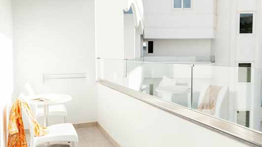 Valkoinen parveke, jossa lasikaide, pöytä ja kaksi tuolia. (Tekoälyn luoma teksti)