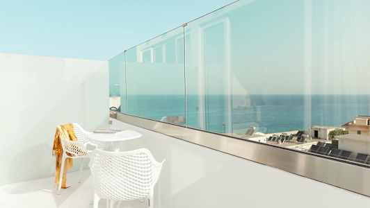 Valkoinen parveke, jossa on kaksi tuolia ja pöytä, näkymä merelle ja rakennuksiin. (Tekoälyn luoma teksti)