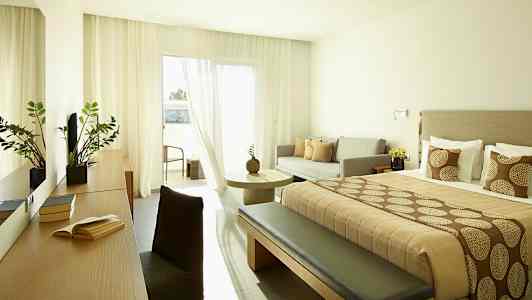 Moderni hotellihuone, jossa parivuode, sohva ja pöytä sekä parveke. (Tekoälyn luoma teksti)