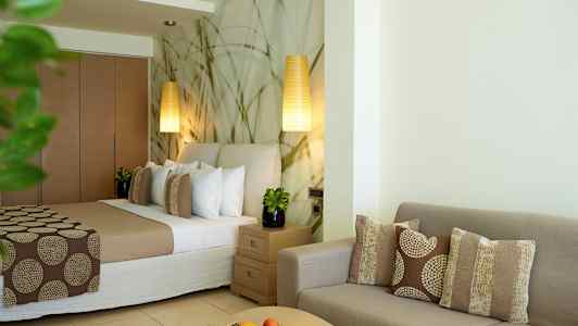 Hotellihuone, jossa sänky, sohva ja pöytä koristeltu tyynyillä ja hedelmillä. (Tekoälyn luoma teksti)