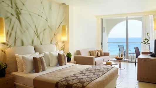 Hotellihuone merinäköalalla ja modernilla sisustuksella, mukaan lukien sänky, sohva ja parveke. (Tekoälyn luoma teksti)