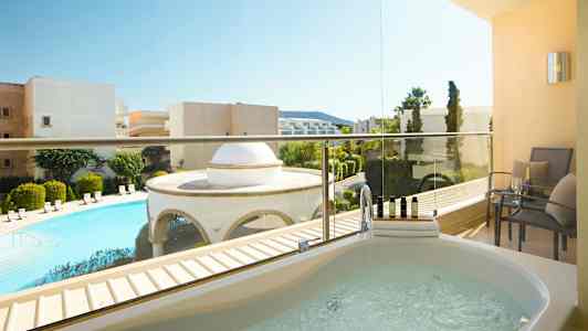 Kuva parvekkeelta, jossa on poreallas ja istuimia. Näkymä uima-altaalle ja ympäröivään rakennuksiin. (Tekoälyn luoma teksti)