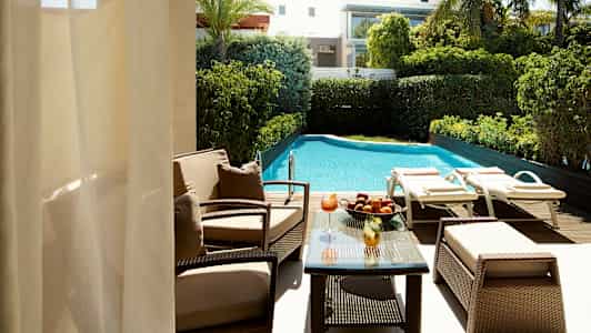 Näkymä uima-altaalle, jossa on aurinkotuoleja ja puutarha, sekä istuinryhmä pöydällä. (Tekoälyn luoma teksti)