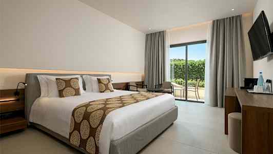 Hotellihuone, jossa suuri vuode, oleskeluryhmä ja lasiovi terassille. (Tekoälyn luoma teksti)