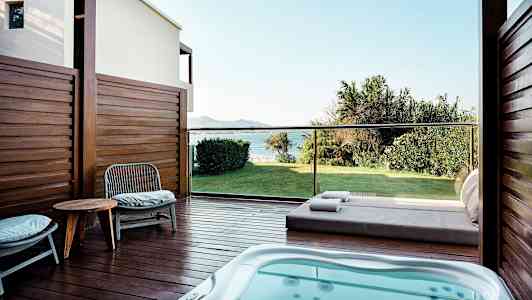 Terassi, jossa poreallas, tuoleja ja pöytä, näkymä vihreälle nurmikolle ja merelle. (Tekoälyn luoma teksti)