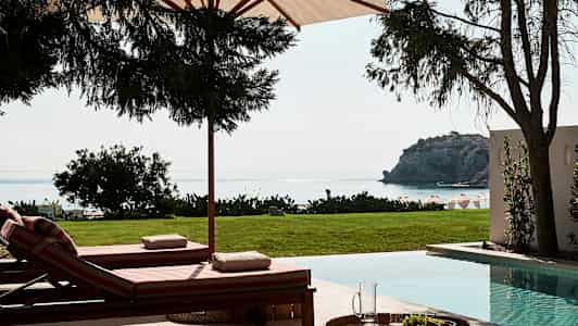 Aurinkotuolit uima-altaan äärellä, näkymä merelle ja kalliolle. (Tekoälyn luoma teksti)