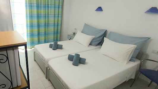 Kuva hotellihuoneesta, jossa on kaksi erillistä sänkyä, valkoiset vuodevaatteet ja siniset sisustuselementit. (Tekoälyn luoma teksti)