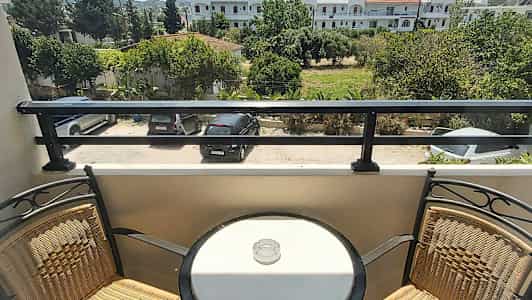 Parveke, jossa kaksi tuolia ja pyöreä pöytä tuhka-astialla, näkymä pysäköintialueelle ja vihreään ympäristöön. (Tekoälyn luoma teksti)