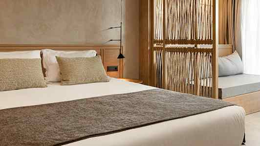 Hotellihuoneen sisustus, jossa on valmistettu sänky ja koristeellinen puinen erottelurakenne. (Tekoälyn luoma teksti)