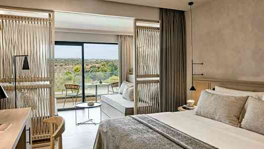 Hotellihuone, jossa on parisänky, istuinalue ja parveke, jolta on näkymä luontoon. (Tekoälyn luoma teksti)