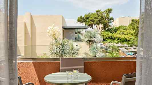 Parveke, jossa pöytä ja tuolit, näkymä puutarhaan, jossa on varjoja. (Tekoälyn luoma teksti)