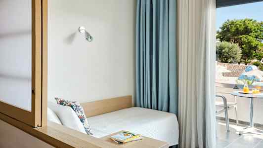 Pieni huone, jossa sänky ikkunan vieressä ja näkymä terassille, jossa pöytä ja tuolit. (Tekoälyn luoma teksti)