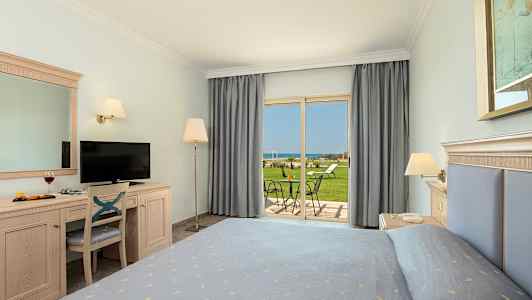 Hotellihuone, jossa on sänky, kirjoituspöytä, televisio ja näkymä puutarhaan sekä merelle. (Tekoälyn luoma teksti)