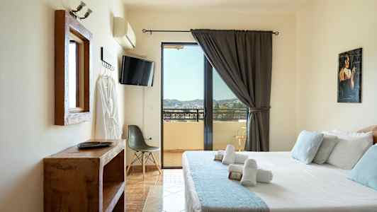 Hotellihuone, jossa on sänky, televisio, tuoli ja näkymä parvekkeelle. (Tekoälyn luoma teksti)